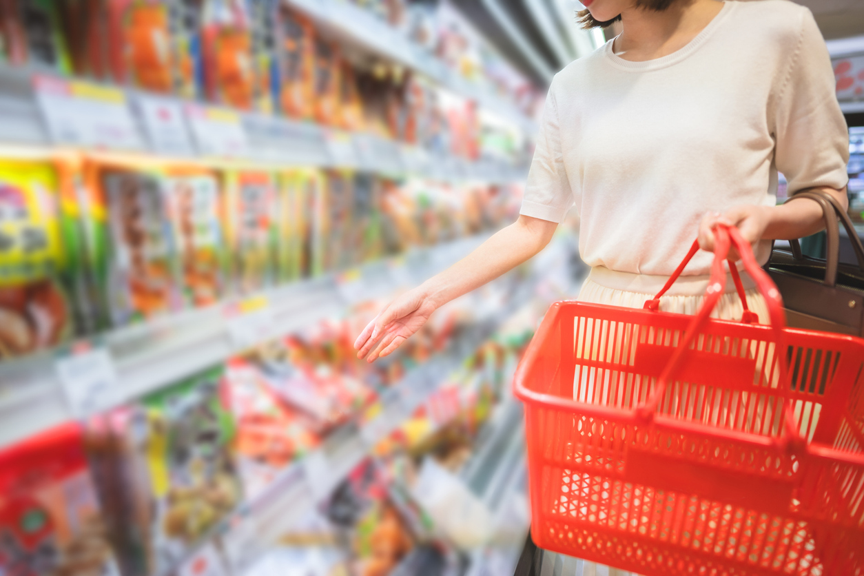 Woman picking something up off convenience store shelf to add to basket