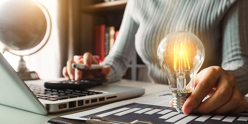 Women working at laptop while holding a glowing light bulb.